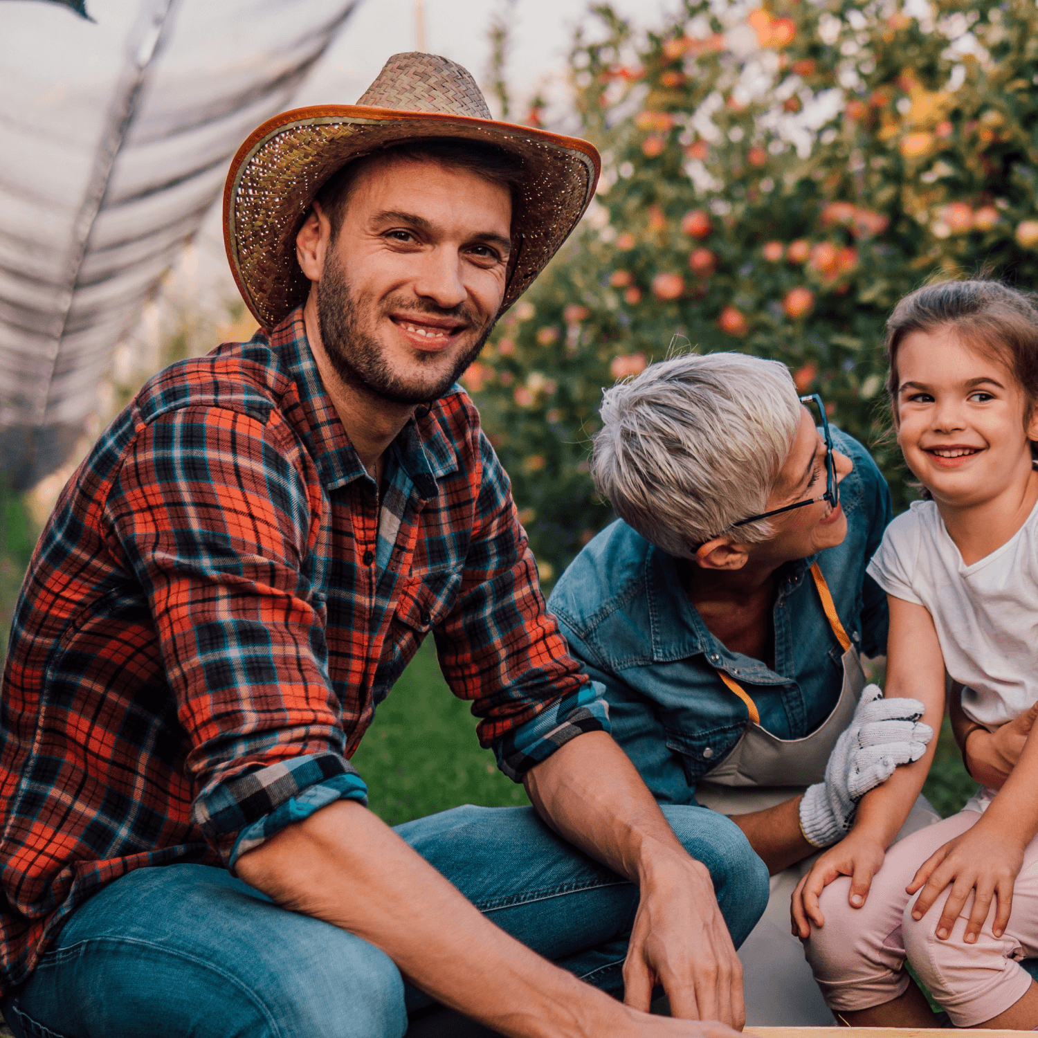 Father, daughter and grandmother in an orchard, smiling.