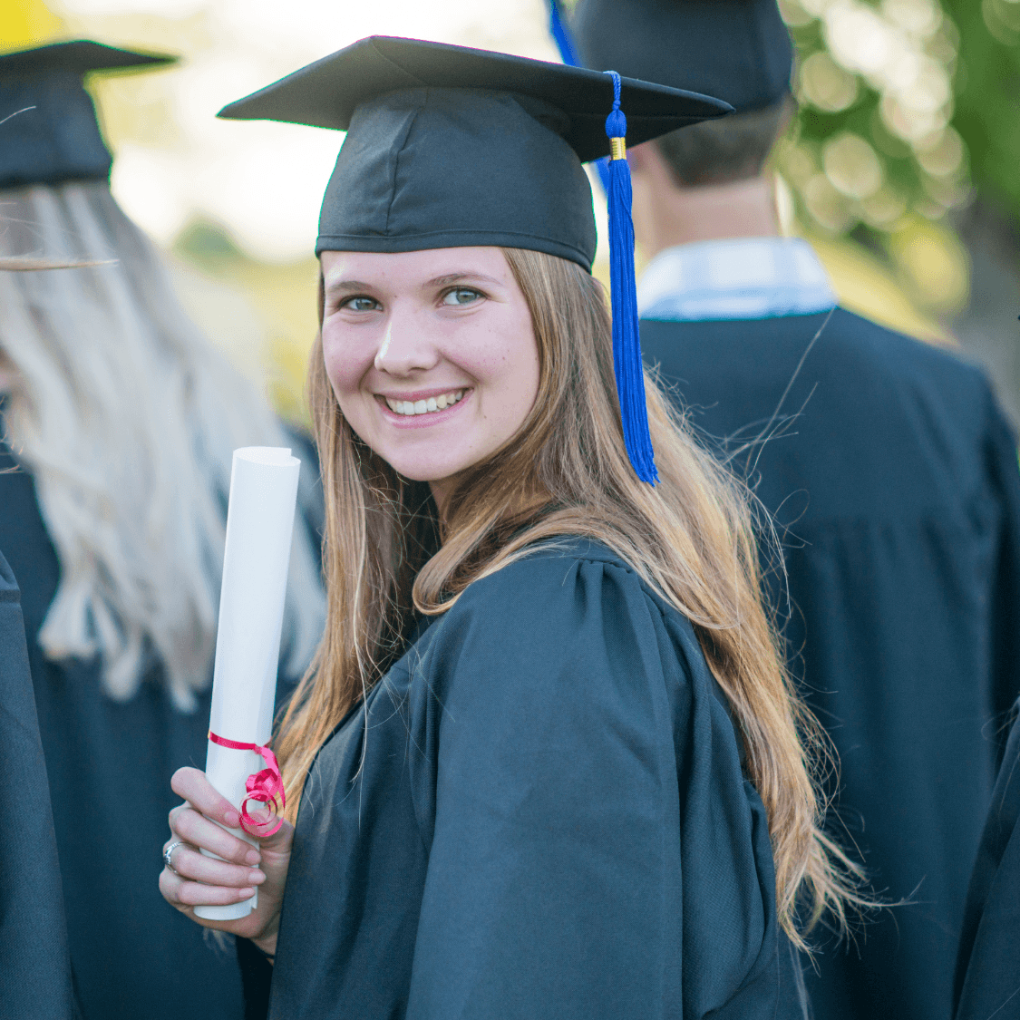 Young girl with blonde hair smiling in graduation hat and gown.