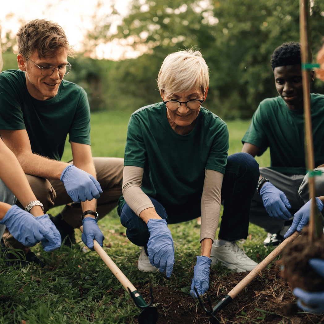 Group of volunteers planting together in a grassy area, wearing gloves and green shirts