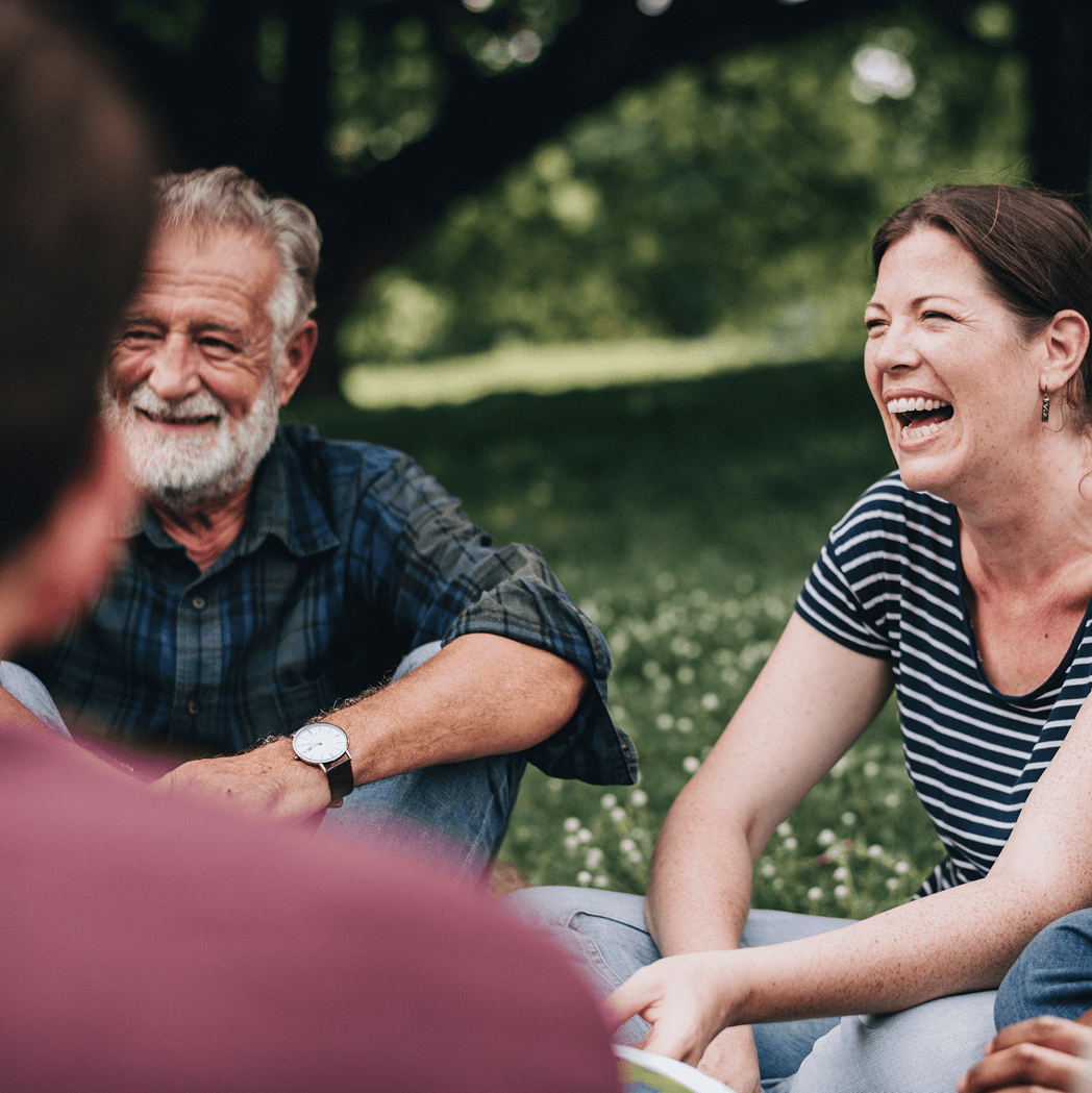 Group of people sitting on grass, laughing and talking together in a park