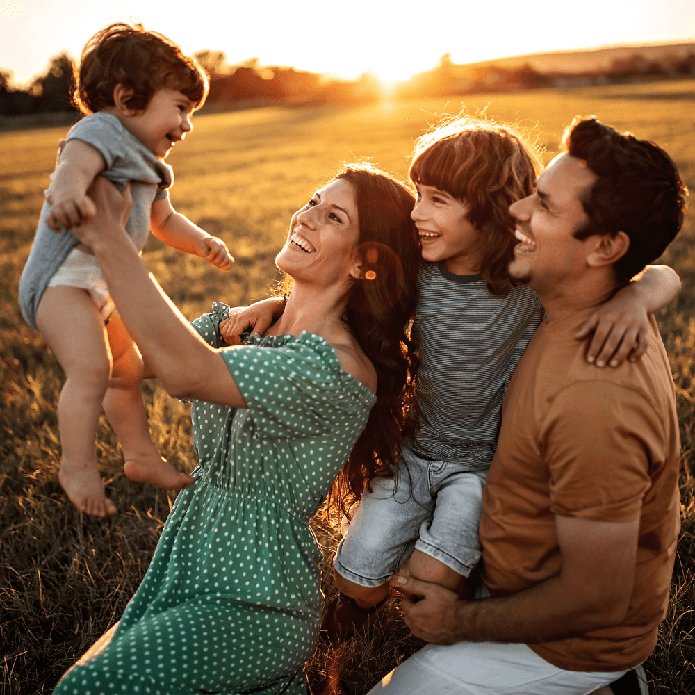 Young couple with two children in a field, smiling.