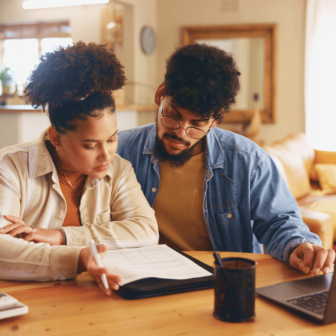Couple reviewing paperwork together at a kitchen table with a laptop open nearby