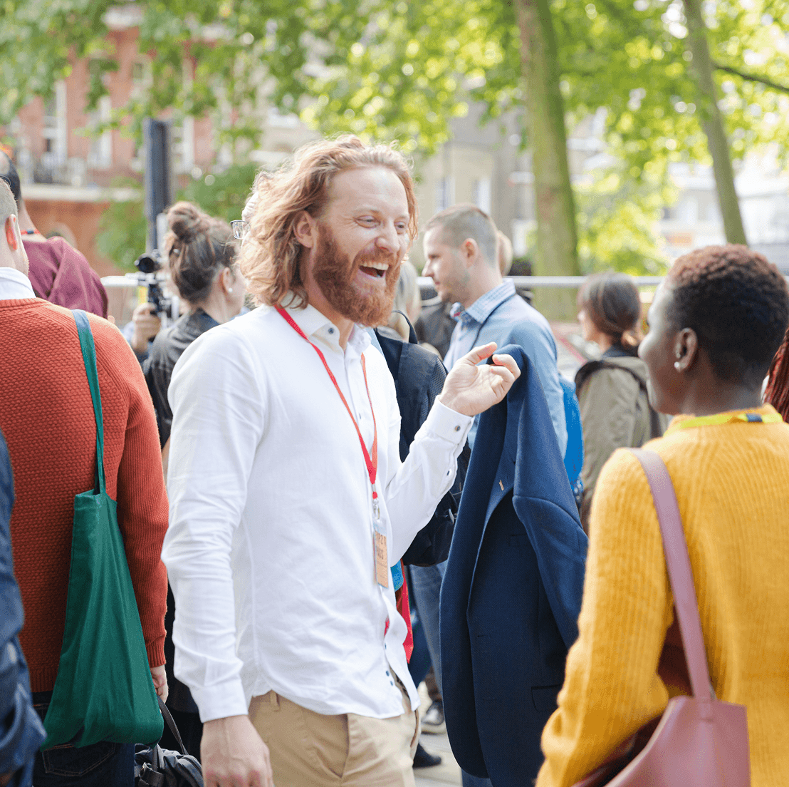 Smiling man with event badge talking with attendees at an outdoor community gathering