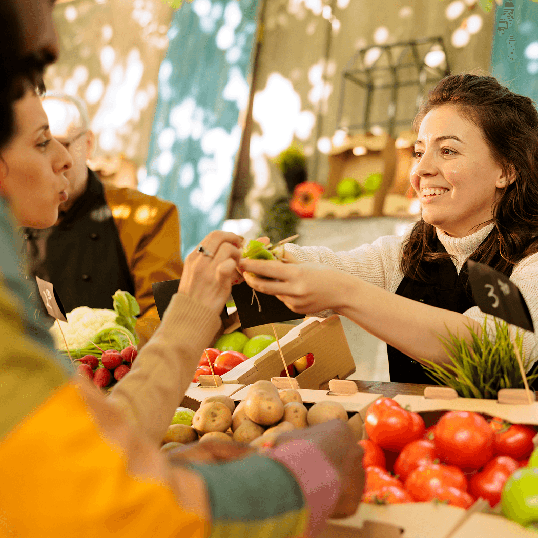 Smiling vendor handing produce to customers at a local farmers market stall