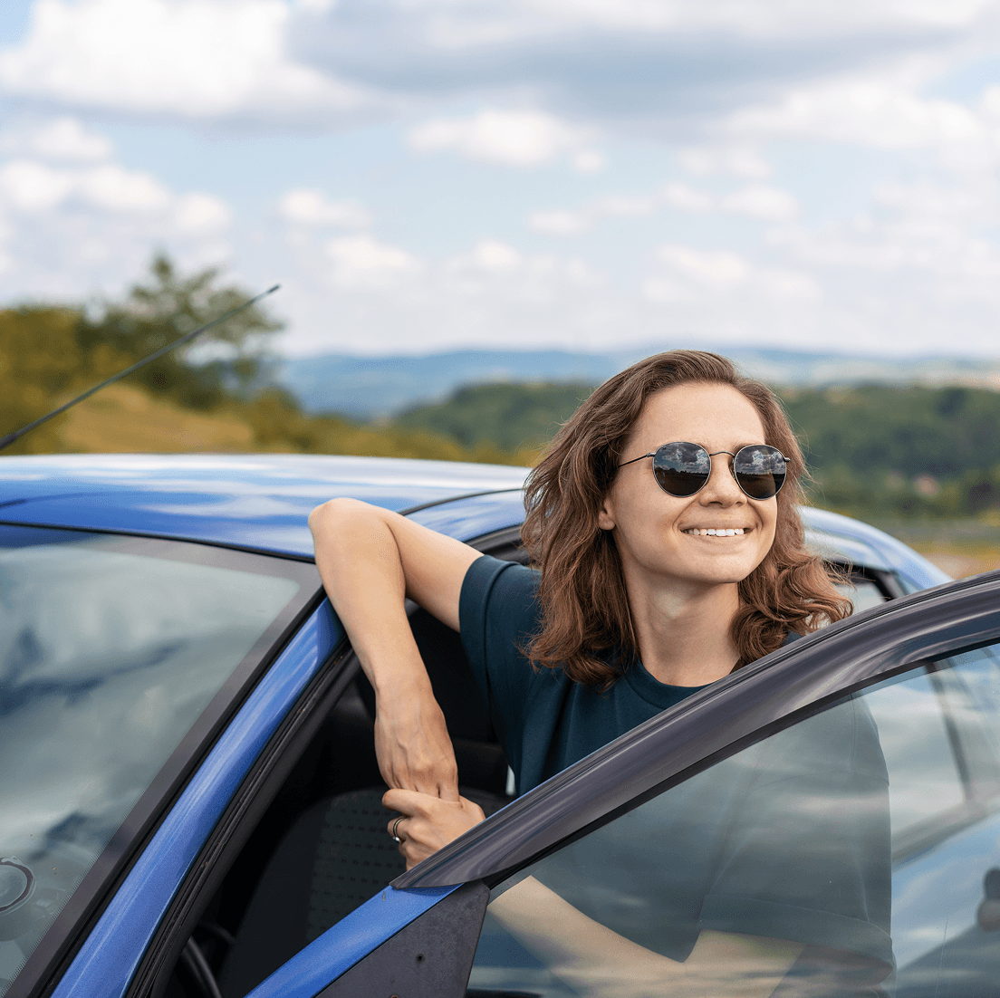 Smiling woman wearing sunglasses standing by her car on a scenic roadside