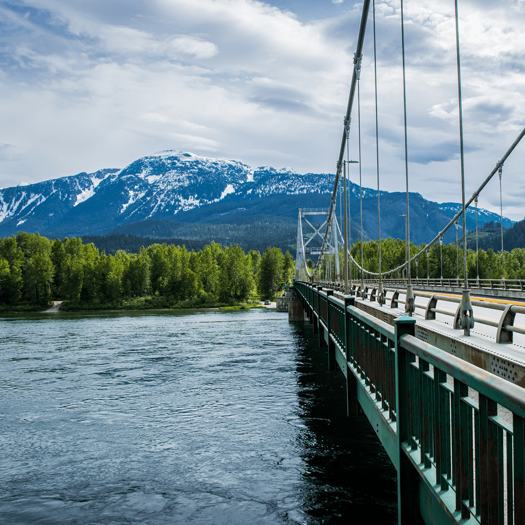 Suspension bridge over Columbia River with snow-capped mountains near Revelstoke, British Columbia